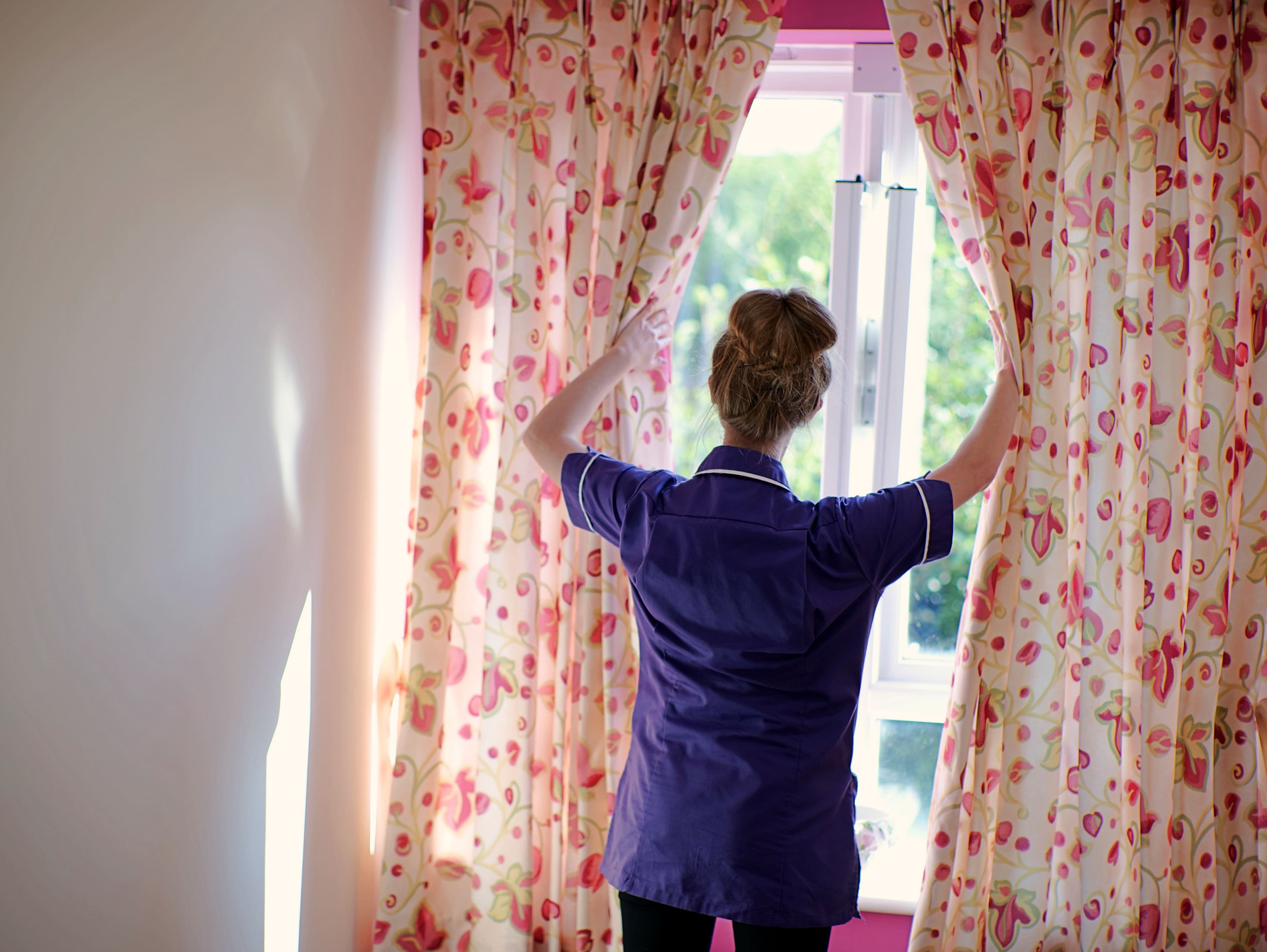 carer opening curtains on a sunny day